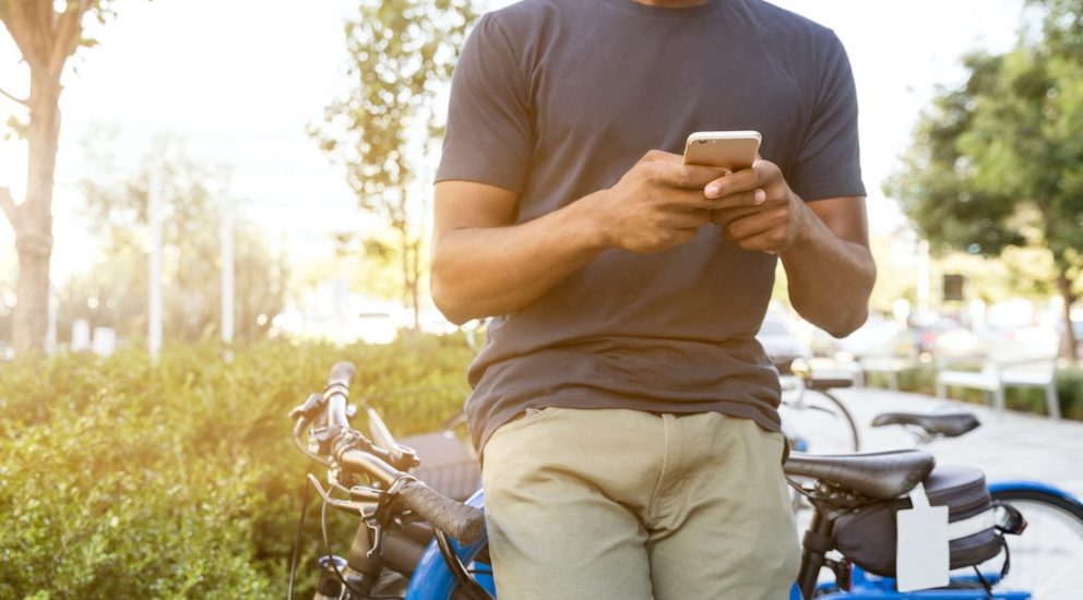 Mann lehnt an einem Fahrrad an und sieht auf sein Smartphone